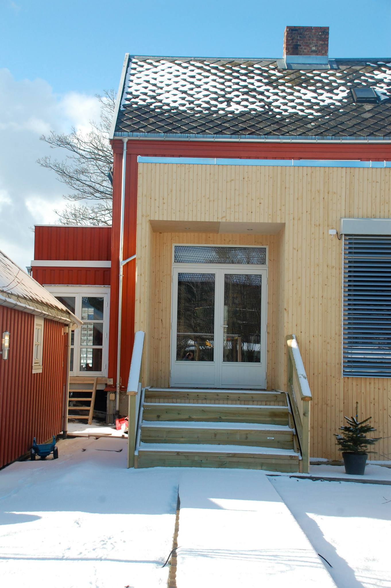 Boligfasade med ny trekledning og trapp opp til inngangsdør, omgitt av snø.