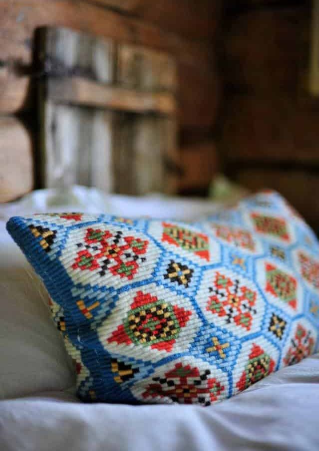 Brodert pute med fargerikt mønster plassert på seng i tømmerhytte.
