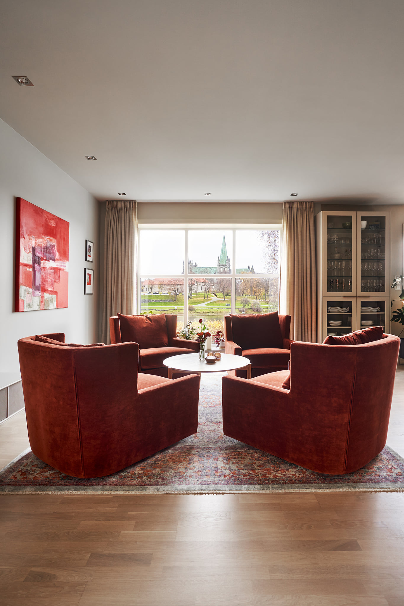 Stue med røde lenestoler, stort vindu og utsikt, innredet i varme og moderne toner.