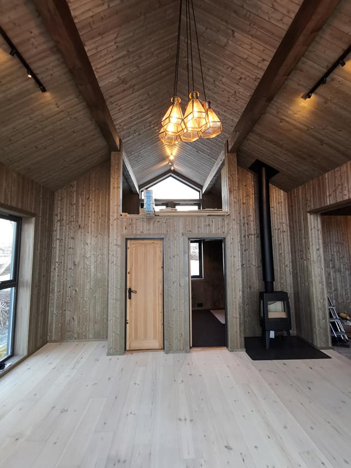 Lys trehytte med åpen takløsning, synlige sperrer og vedovn.