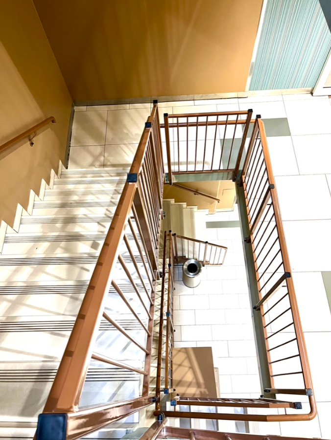 Trappeoppgang med trehåndløper og lyse vegger, sett ovenfra i moderne bygg.