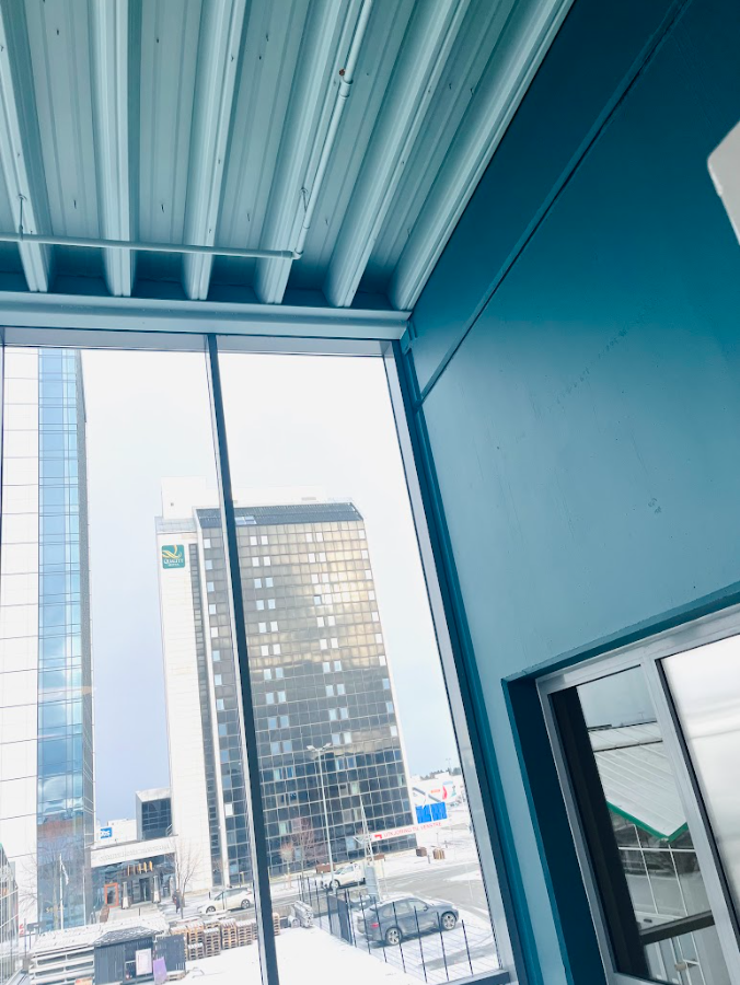 Blått interiør med store vindusflater og utsikt mot moderne kontorbygg.